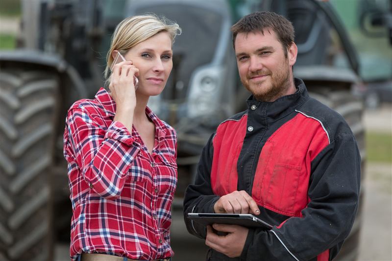 Zwei Landwirte mit Tablet und Smartphone vor einem Traktor